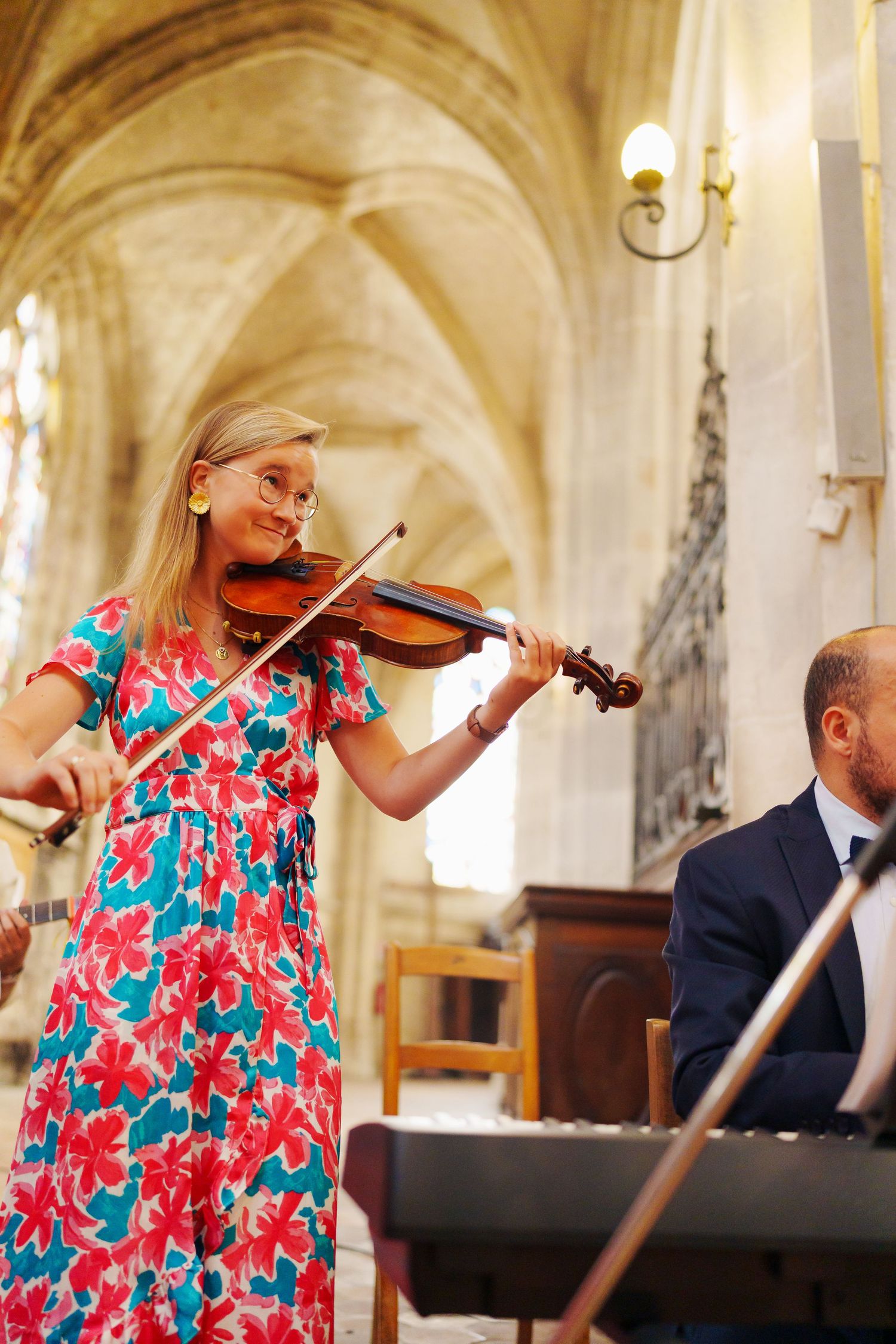 Musician in floral dress performs on violin during church wedding ceremony.