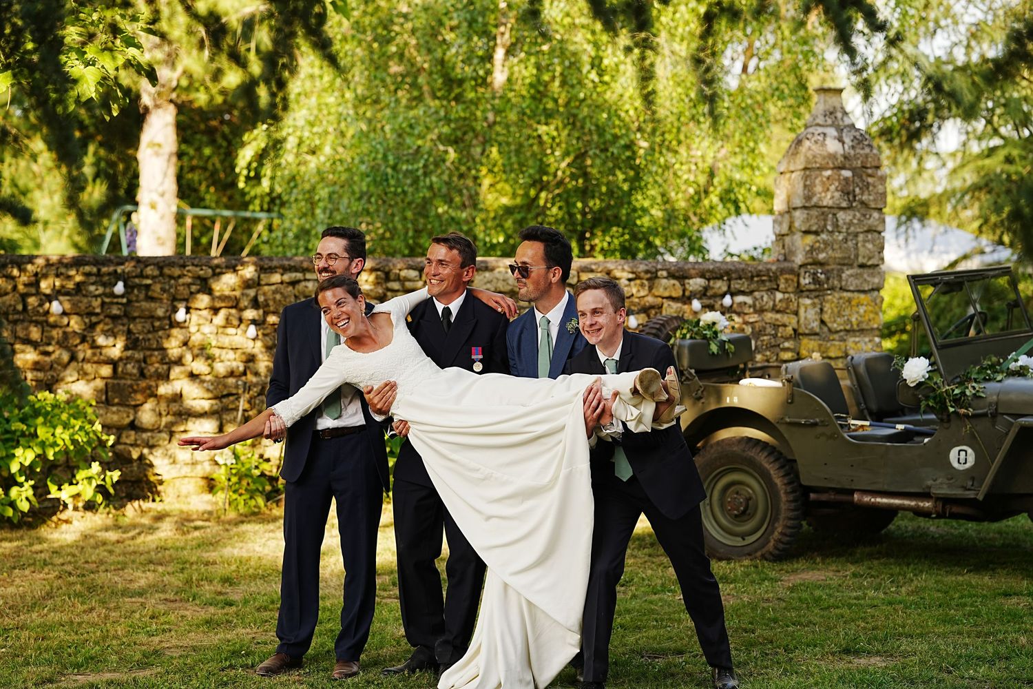 Wedding party poses for photos in a lush garden setting with natural sunlight.