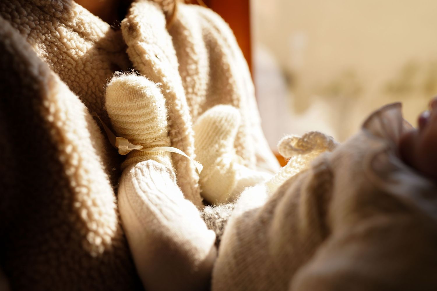 Close-up of tiny baby feet wrapped in soft white knitted booties.