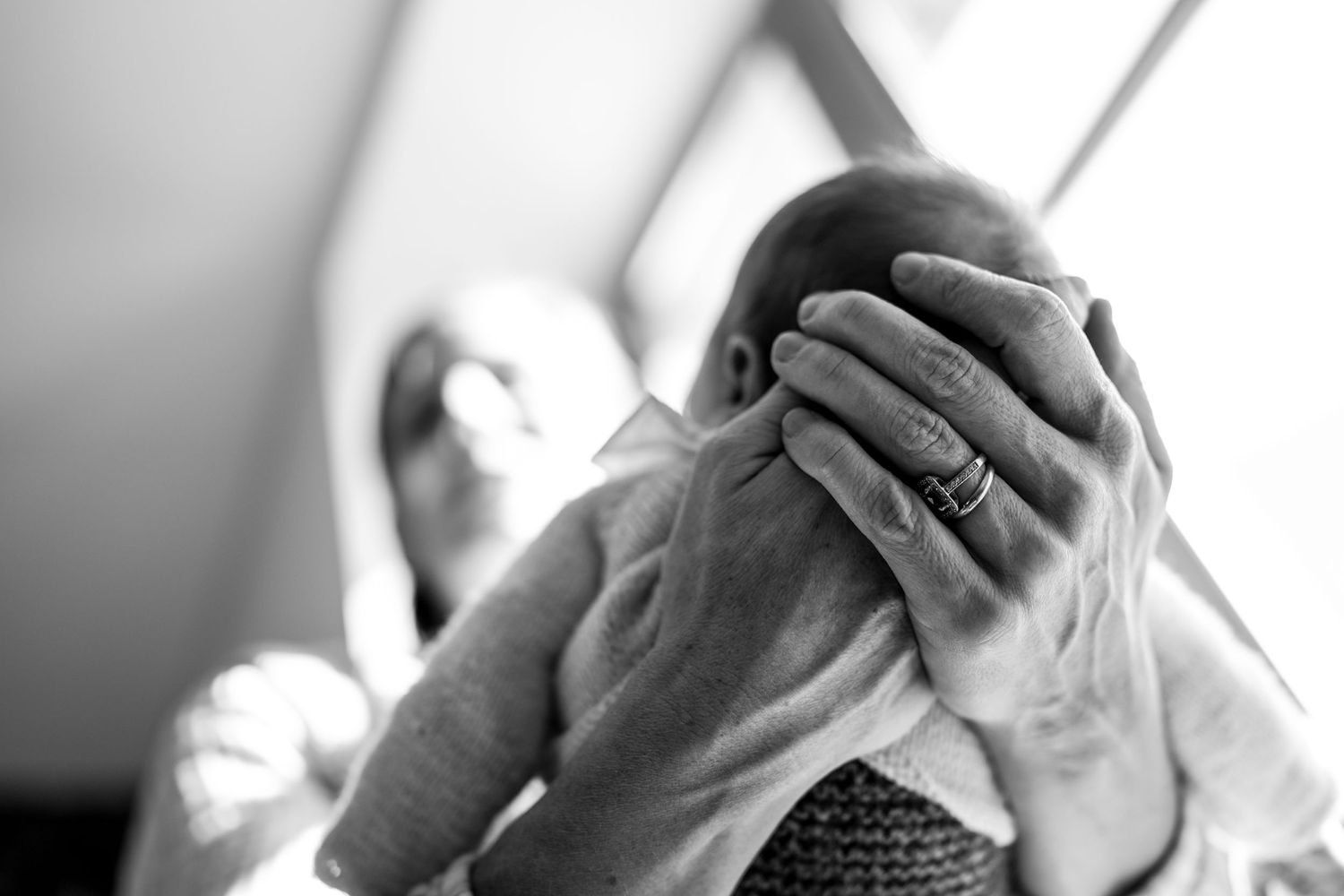 Close-up black and white image of gentle hands cradling a newborn baby's head.