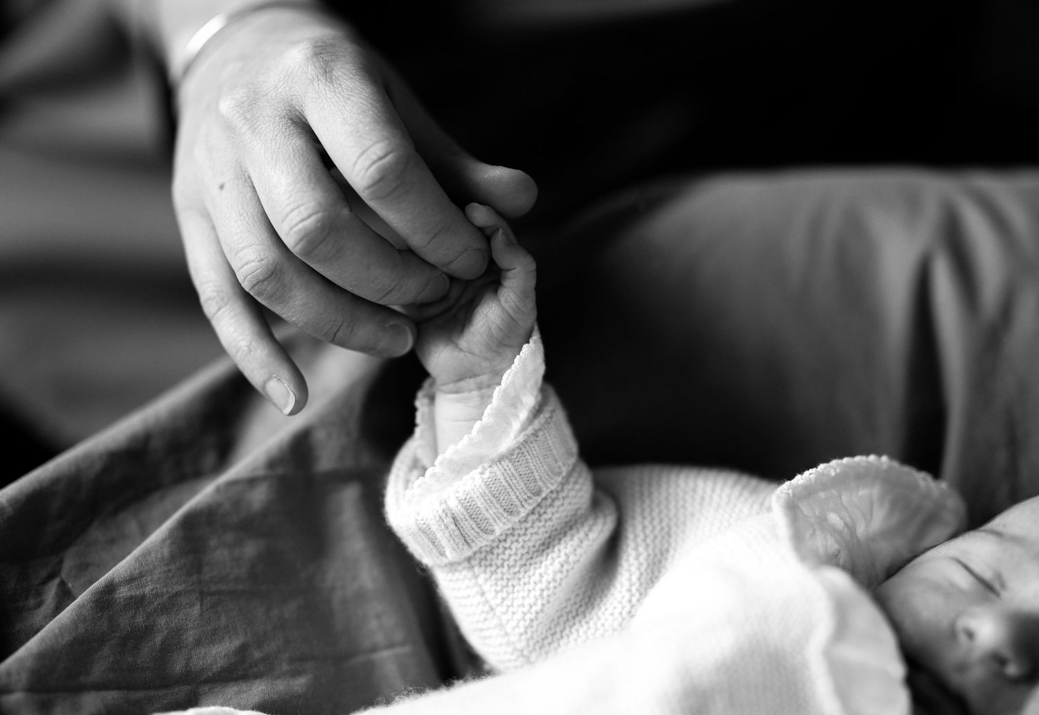 Black and white close-up shots of gentle hands holding a newborn baby.