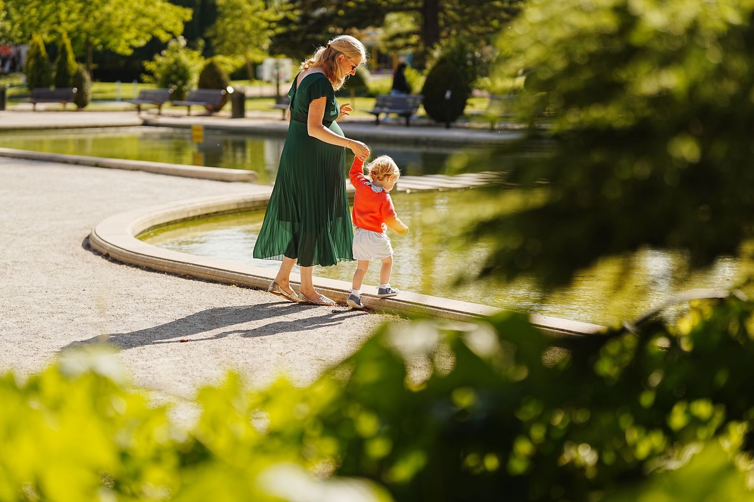 People walking through lush green park pathway on sunny day.