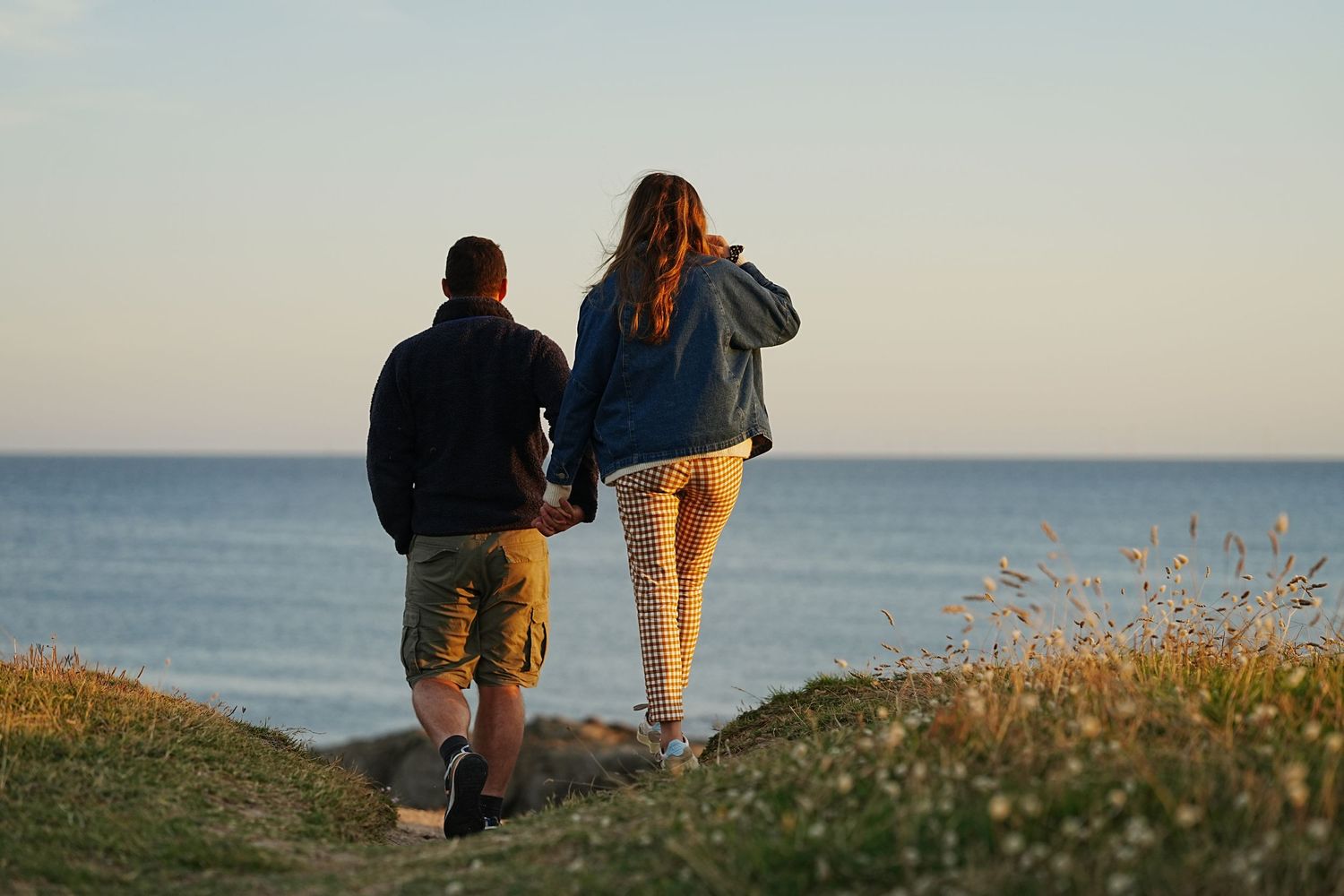 People walking along scenic coastal path during golden hour.
