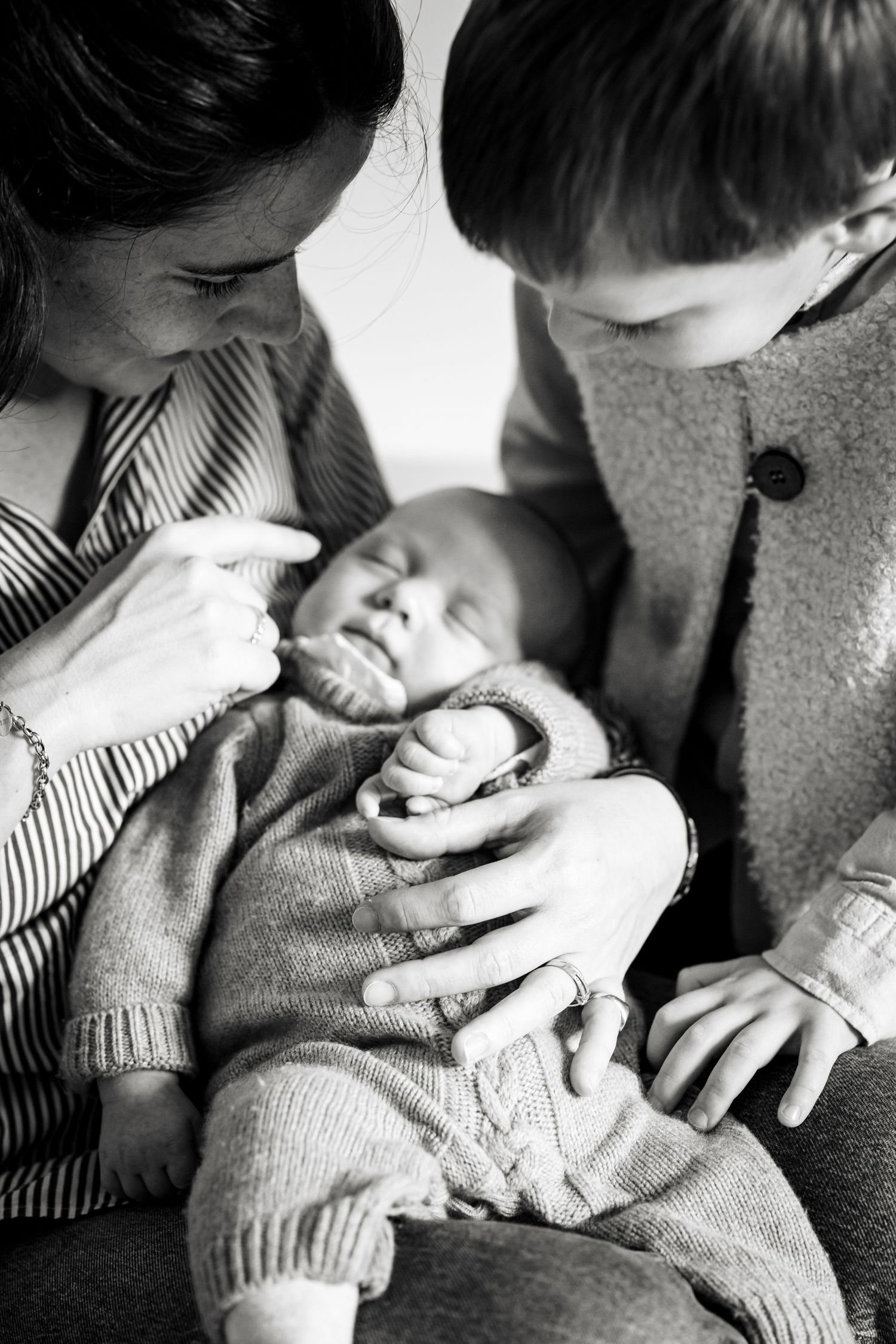 Black and white photo of a mother and young boy tenderly holding a sleeping newborn baby.