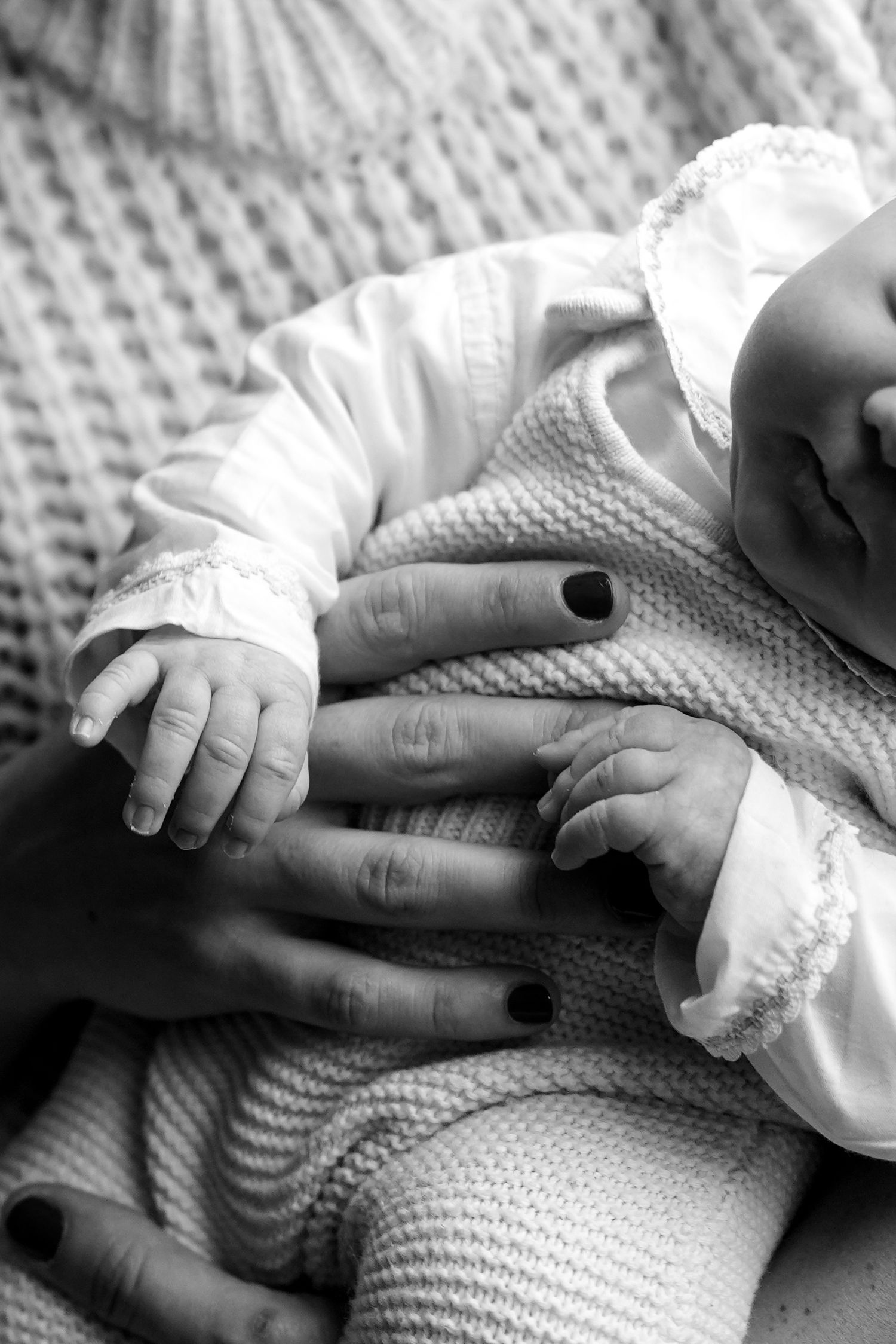 Close-up black and white image of tiny baby hands on textured knit fabric.