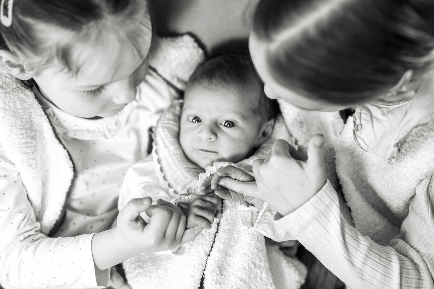 Black and white photo of a newborn baby being held by two young children, looking up with wide eyes.