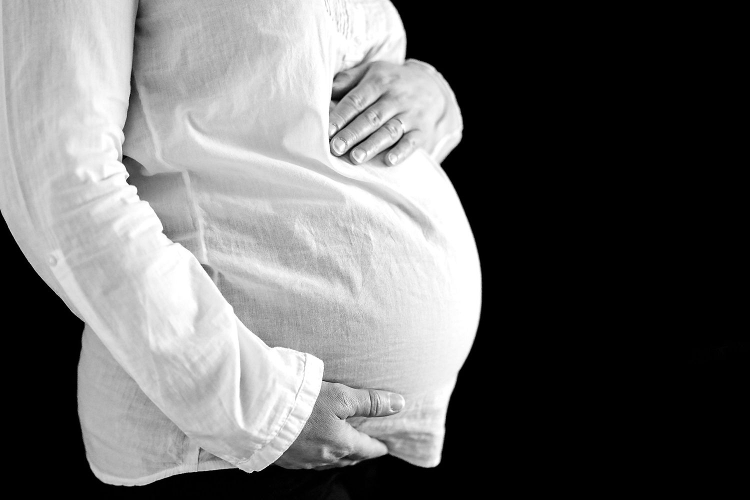 Side view of pregnant belly in white clothing against dark background.