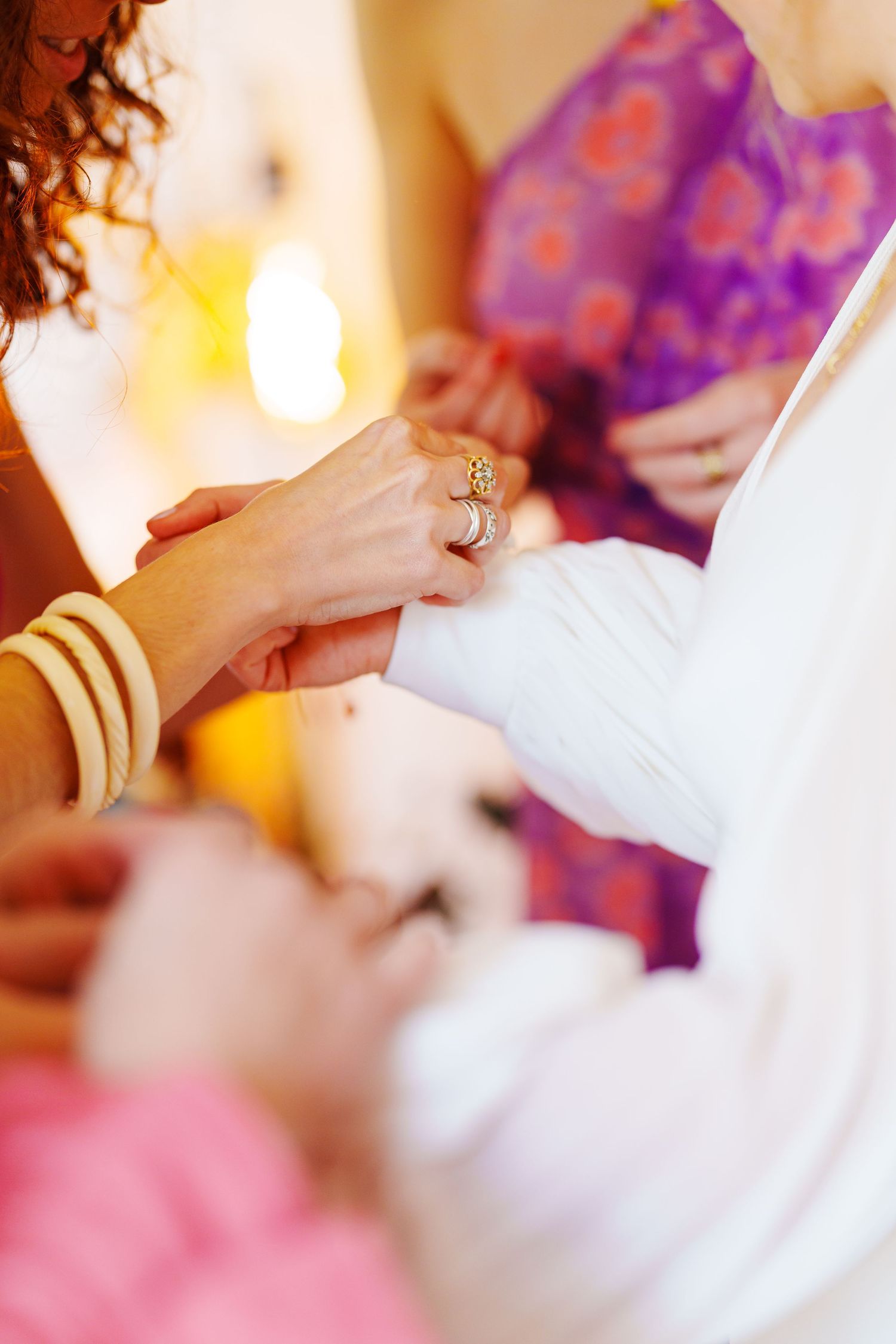 Close-up view of hands exchanging wedding rings during an intimate ceremony with soft purple lighting.