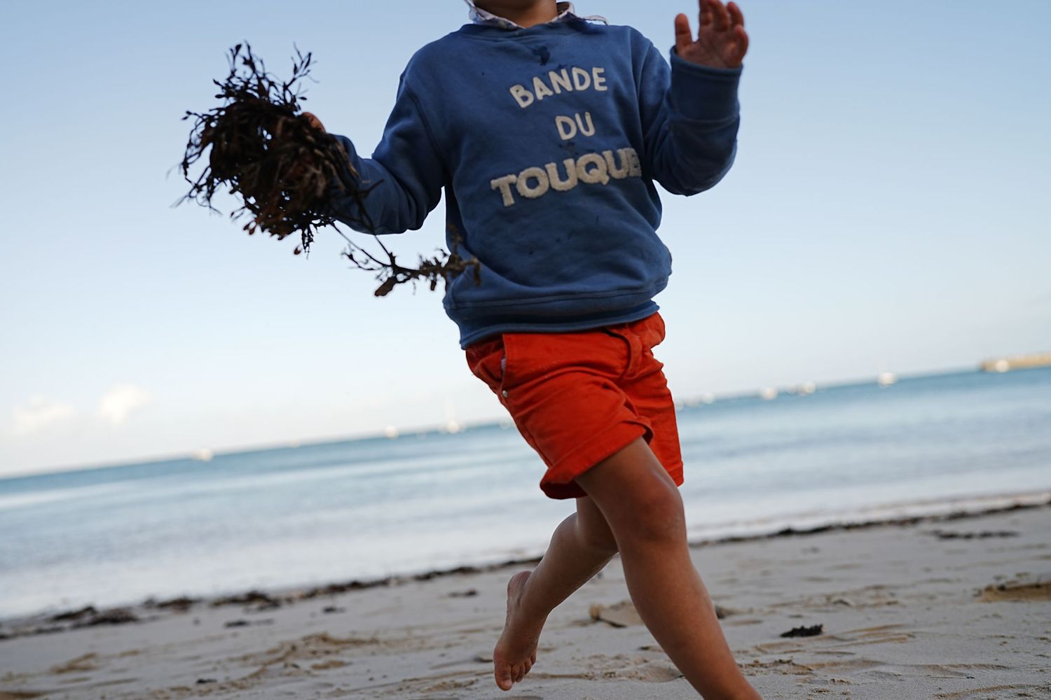Person wearing a blue shirt and orange shorts runs along the beach.