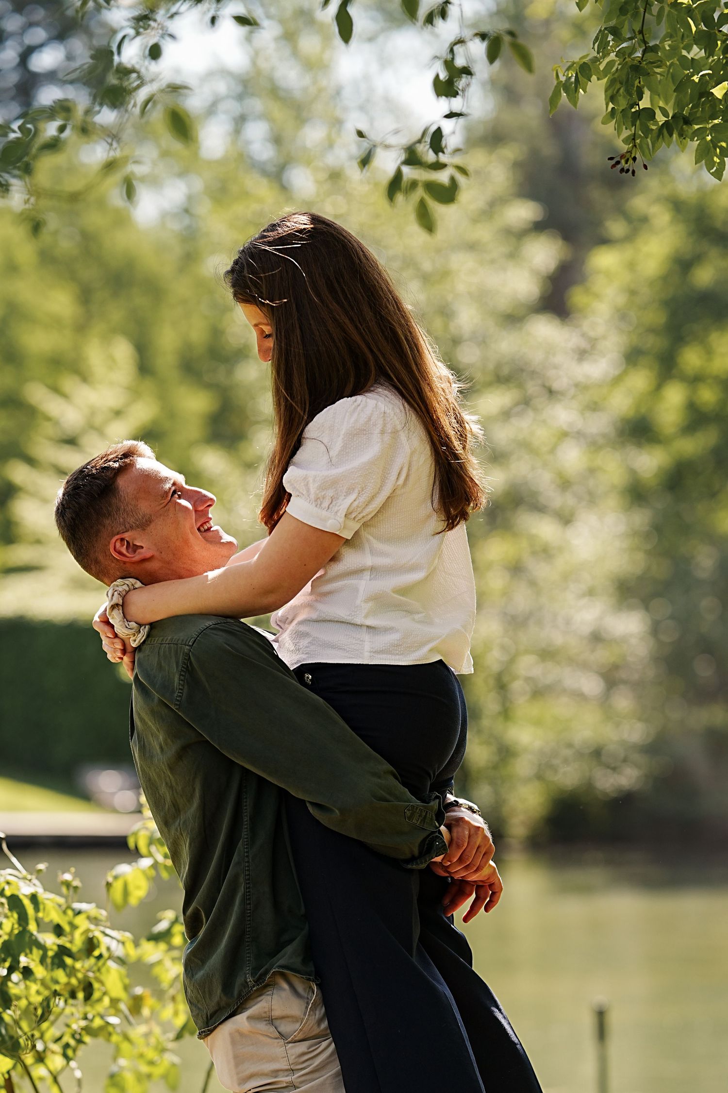 A romantic couple embracing by a lake on a sunny afternoon.