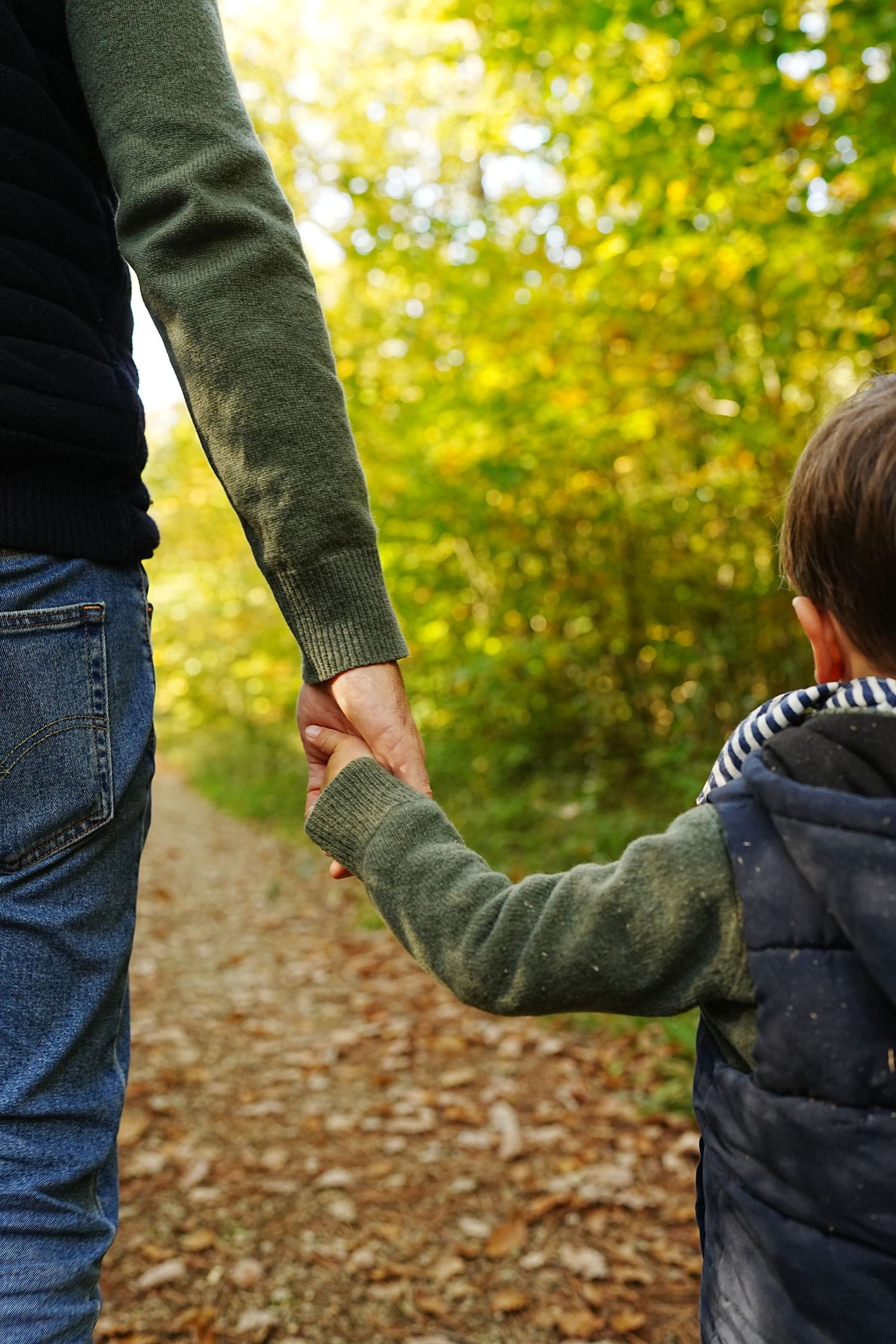 Adult and child walking together on an autumn path covered in fallen leaves.