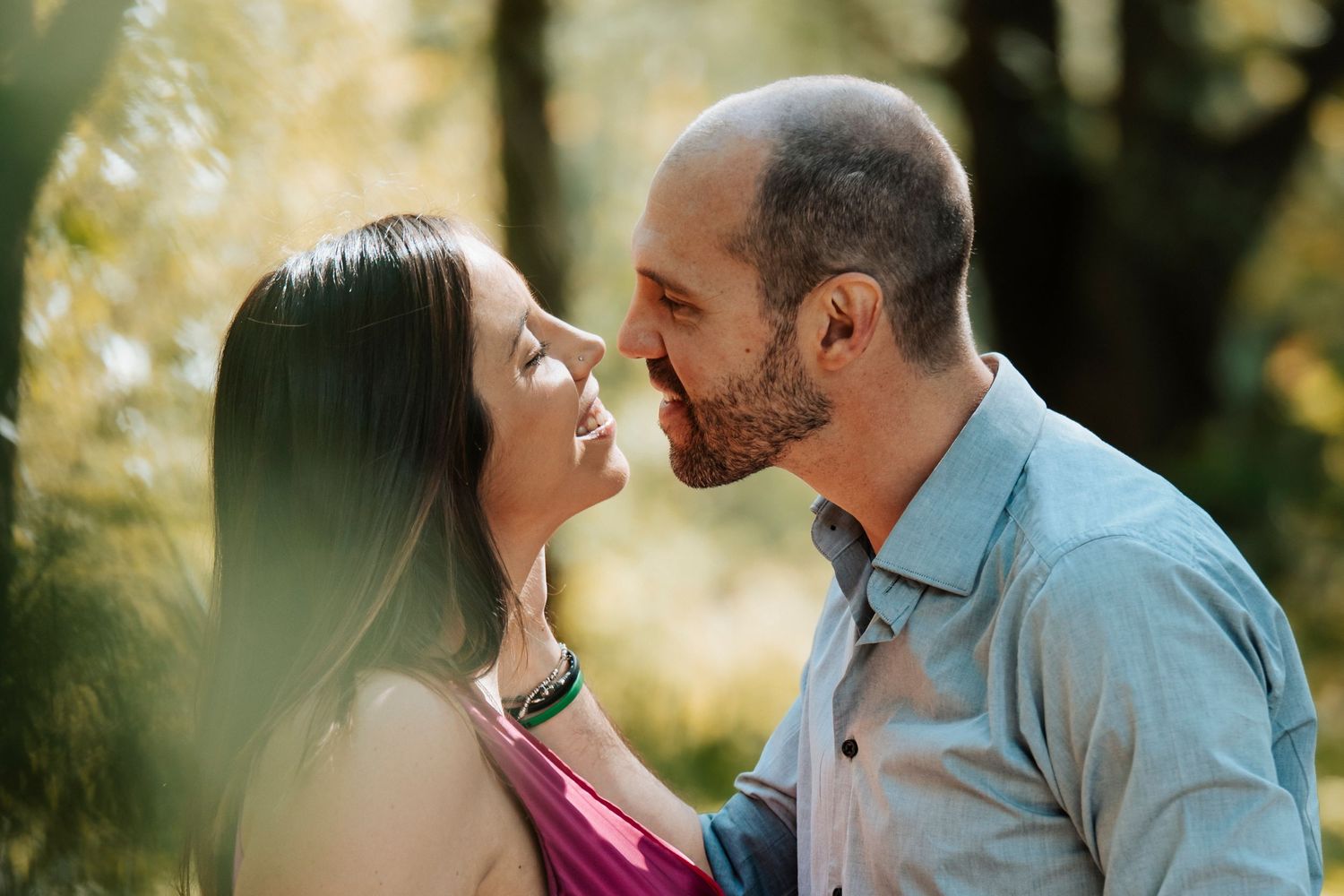 Couple sharing a tender nose-to-nose moment surrounded by bright sunlit trees in a forest.
