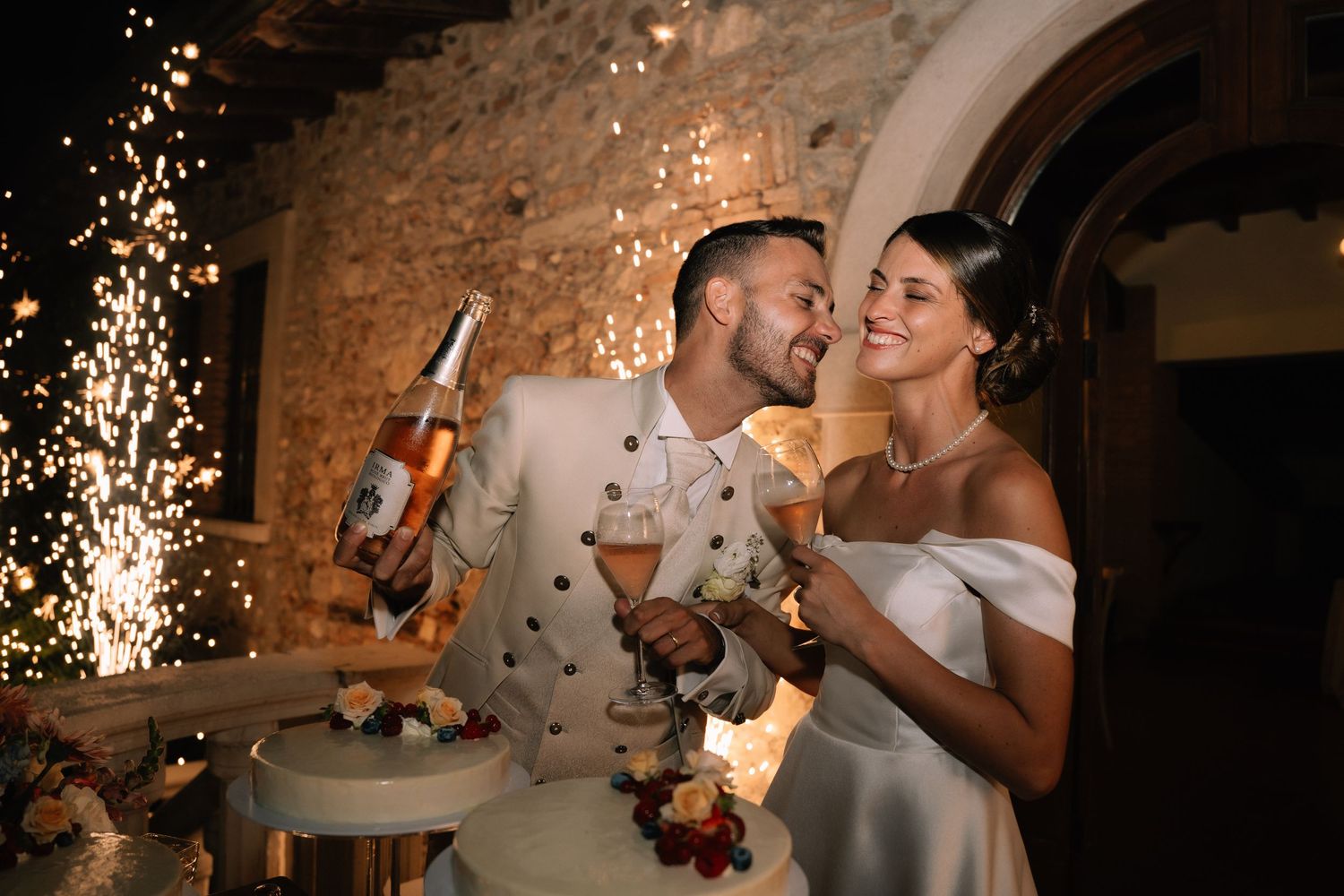 Bride and groom celebrating with champagne and sparklers at elegant outdoor wedding reception at night.
