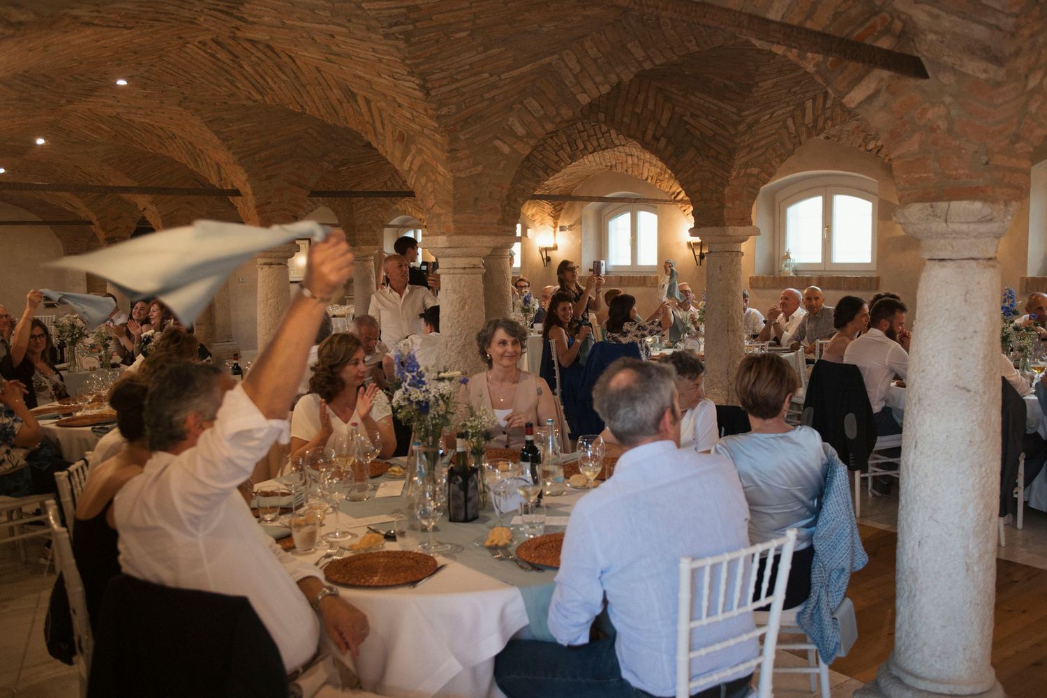 Guests celebrating at a wedding reception in a stunning stone-arched venue with elegant table settings.