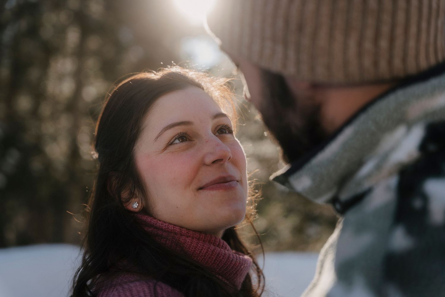 Woman smiling warmly at her partner in a sunlit snowy winter outdoor setting.