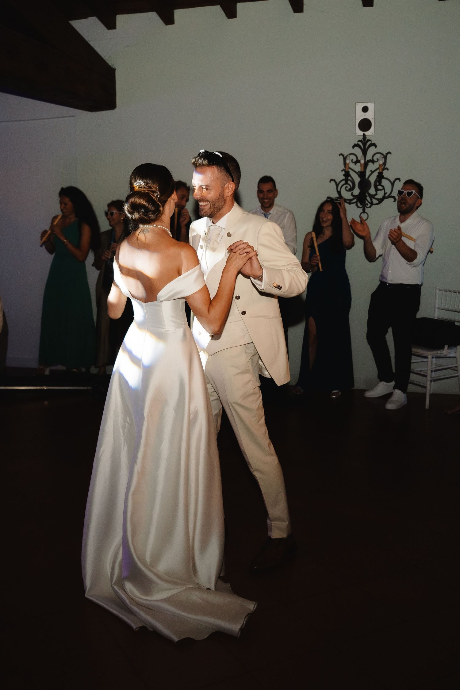 Bride and groom share their first dance at wedding reception, surrounded by guests applauding in elegant venue.
