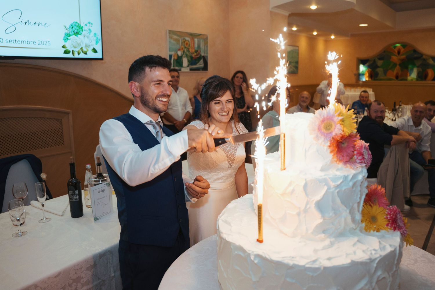 Bride and groom cut their elegant white wedding cake with sparklers at their reception.