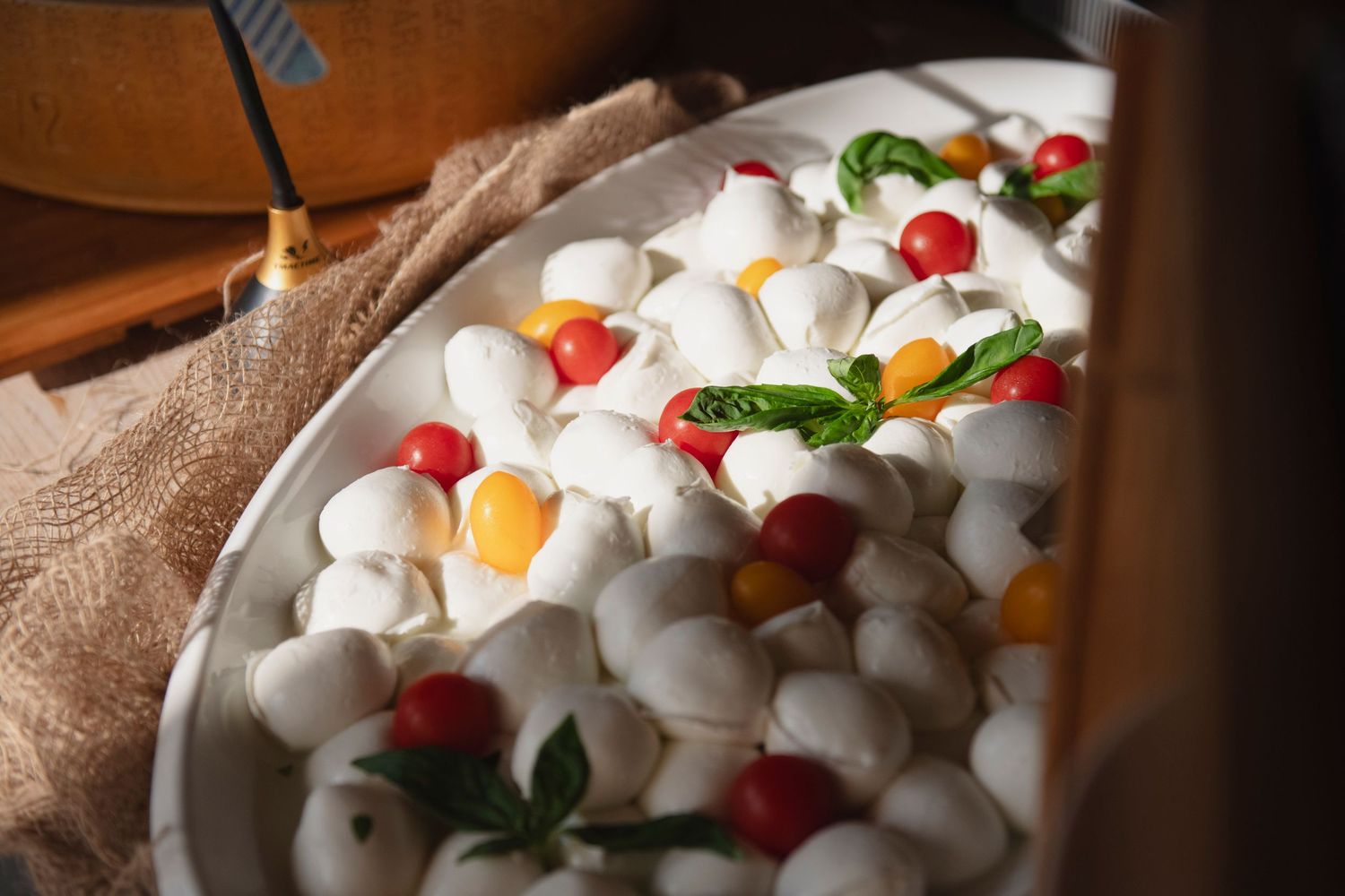 Fresh mozzarella balls with colorful cherry tomatoes and basil leaves on white serving platter.
