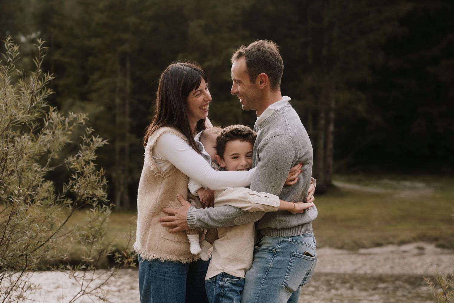 Happy family of four sharing a warm embrace outdoors with a forest backdrop.