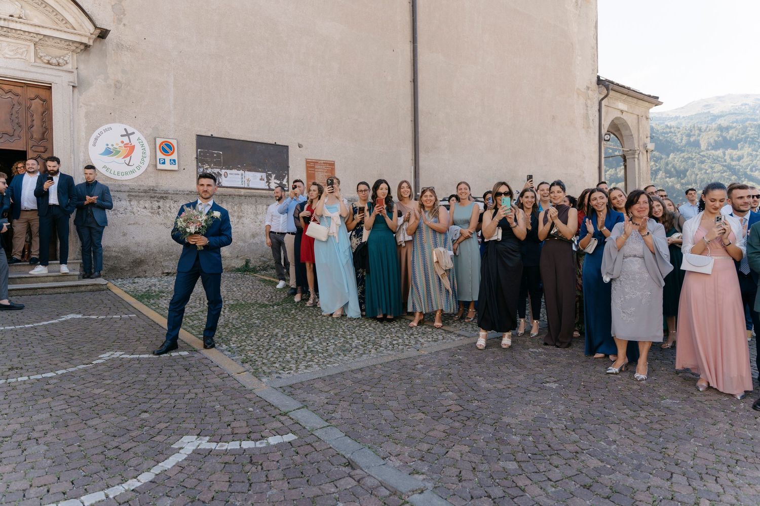 Wedding guests applauding outside a historic Italian church during a wedding celebration on a cobblestone square.