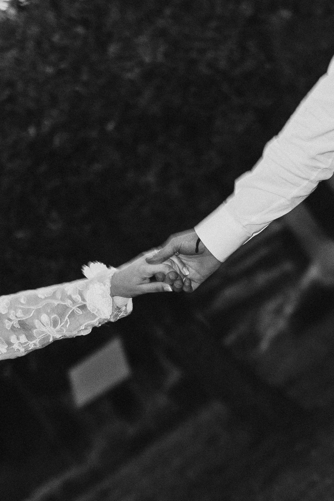 Foto in bianco e nero in primo piano di una sposa e uno sposo che si tengono per mano durante la cerimonia nuziale.