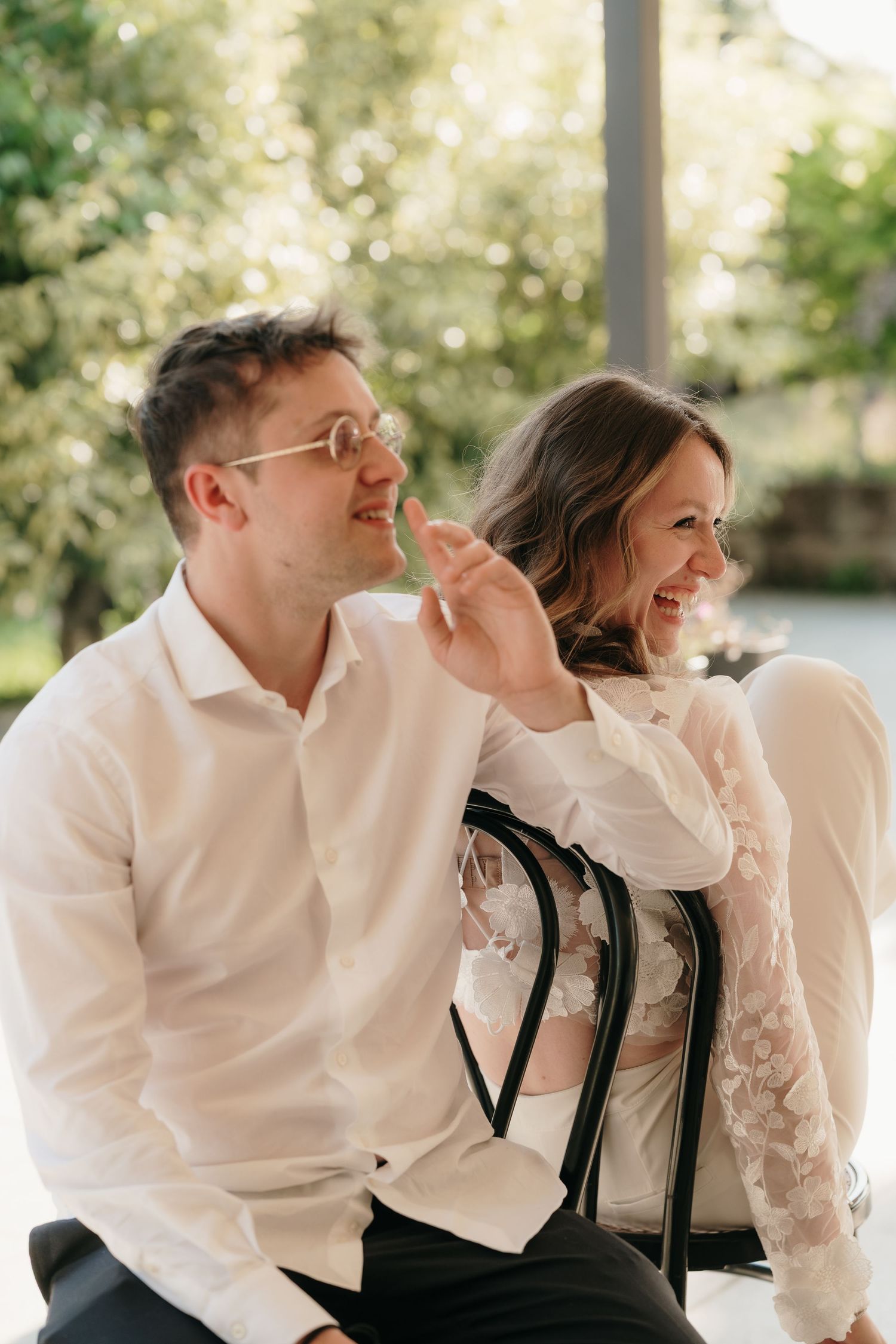 Happy couple sitting together laughing at a wedding ceremony outdoors in natural light.