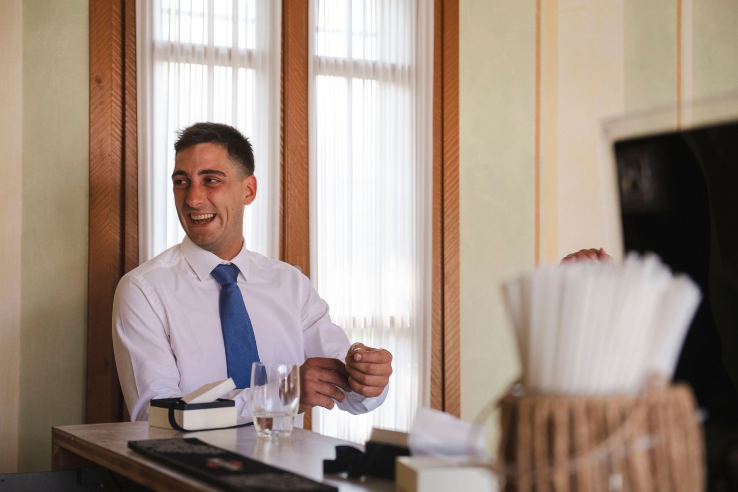 Smiling groom in white shirt and blue tie standing at reception table on wedding day.