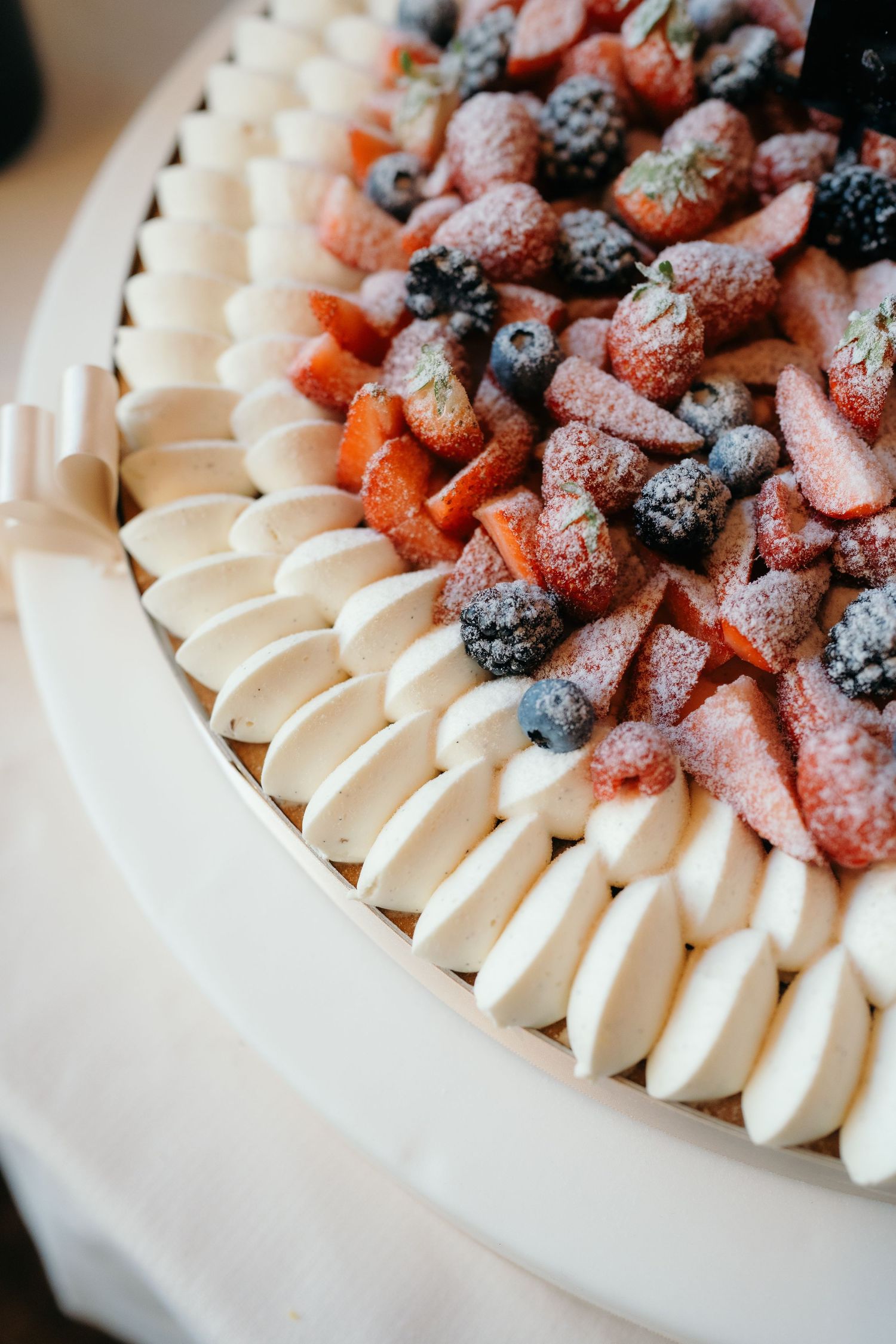 Elegant wedding cake topped with fresh strawberries and blueberries dusted with powdered sugar.
