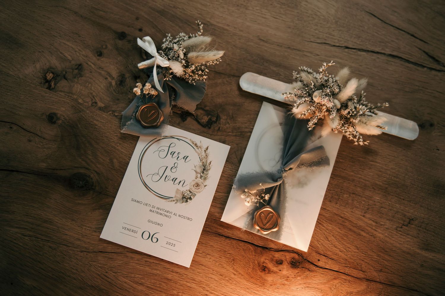 Elegant wedding stationery flat lay with floral accents, wax seal, and rings on rustic wood.
