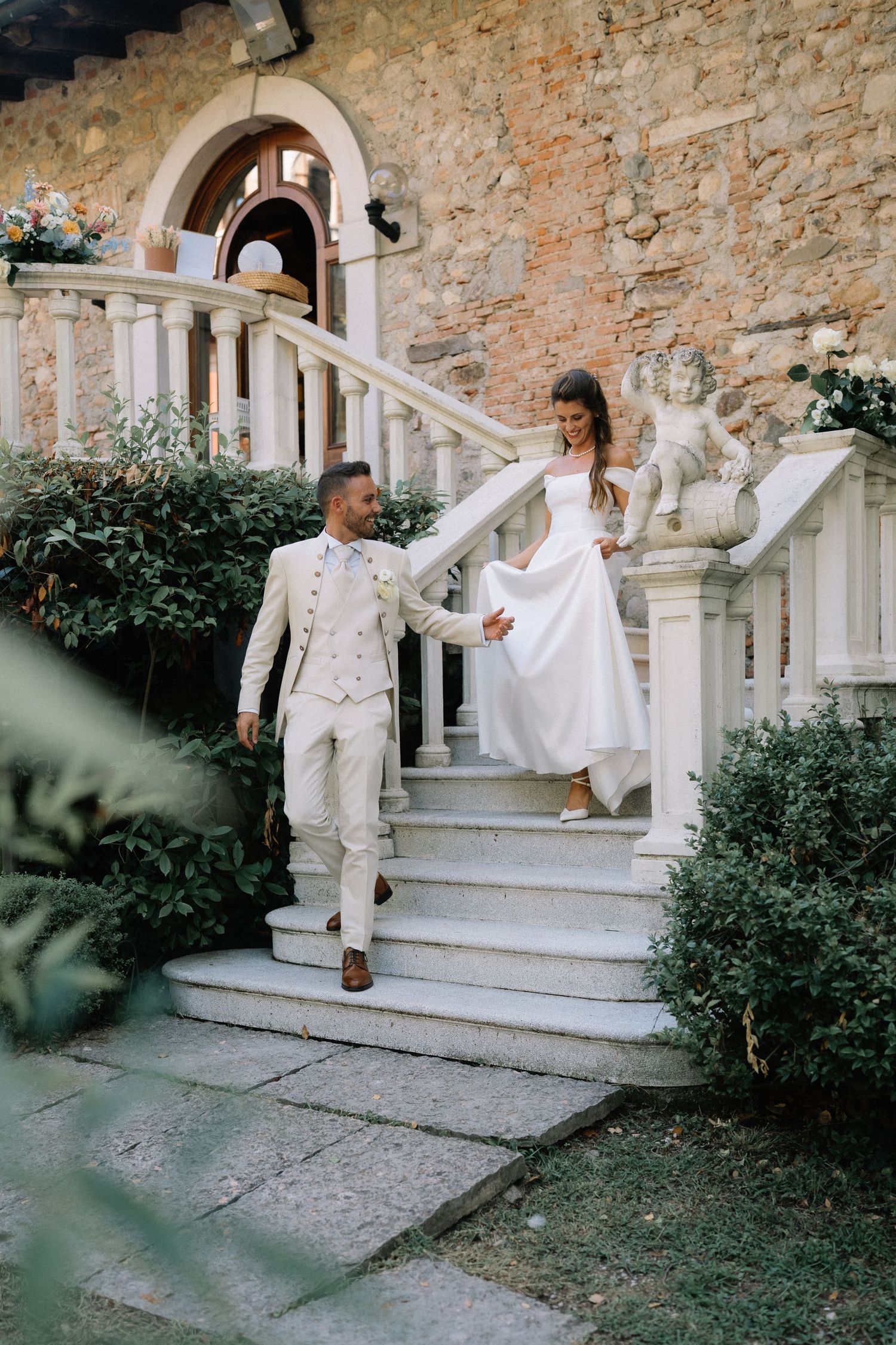 Bride and groom descend elegant white stone stairs at a rustic Italian villa on their wedding day.