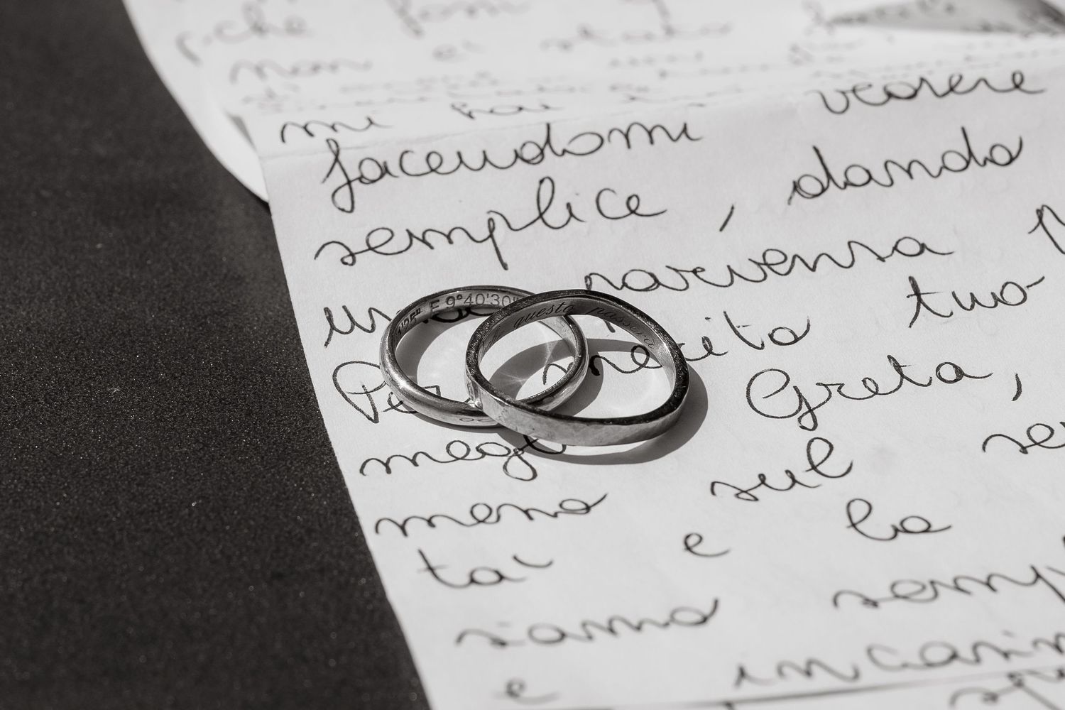 Two silver wedding rings resting on a handwritten love letter in Italian, symbolizing romance and commitment.