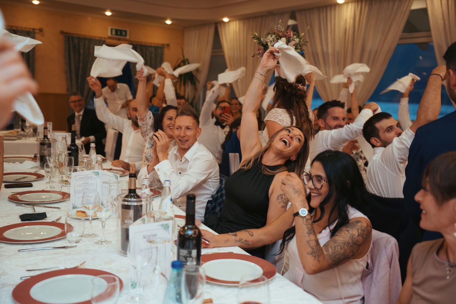 Wedding guests joyfully wave white napkins in celebration at a lively wedding reception dinner party.