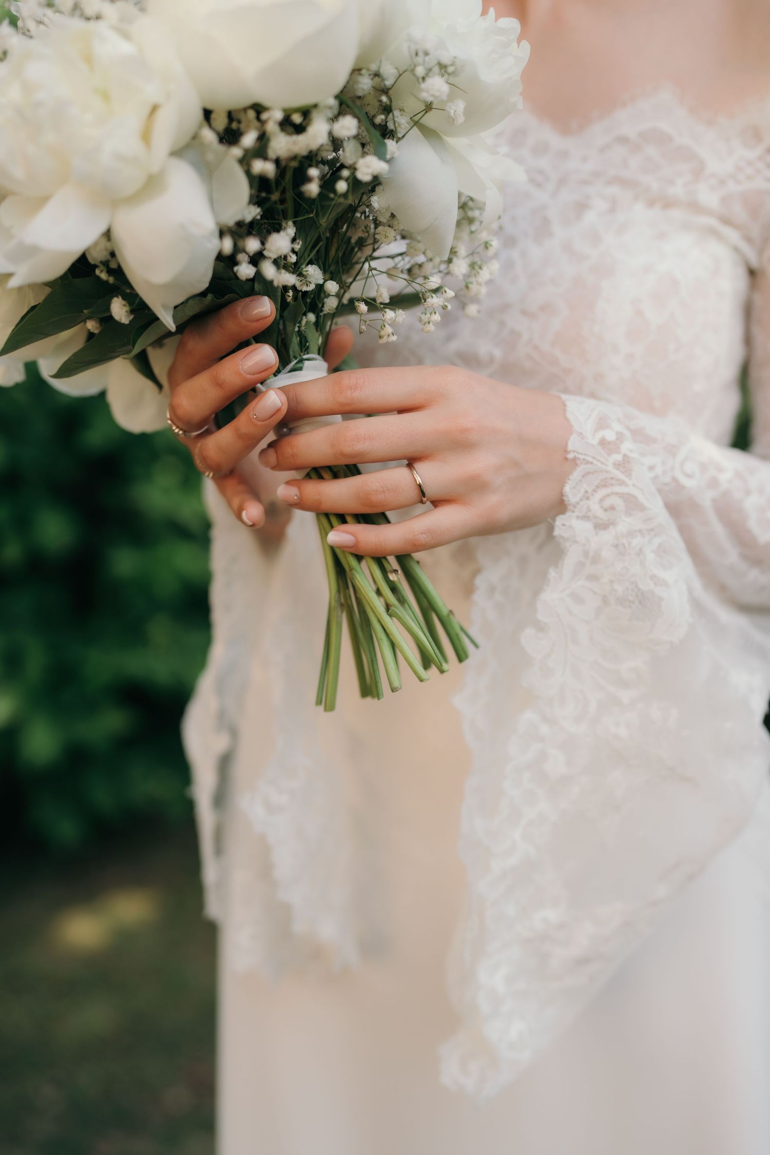 Bride in white lace wedding dress holding a beautiful bouquet of white peonies and baby's breath.