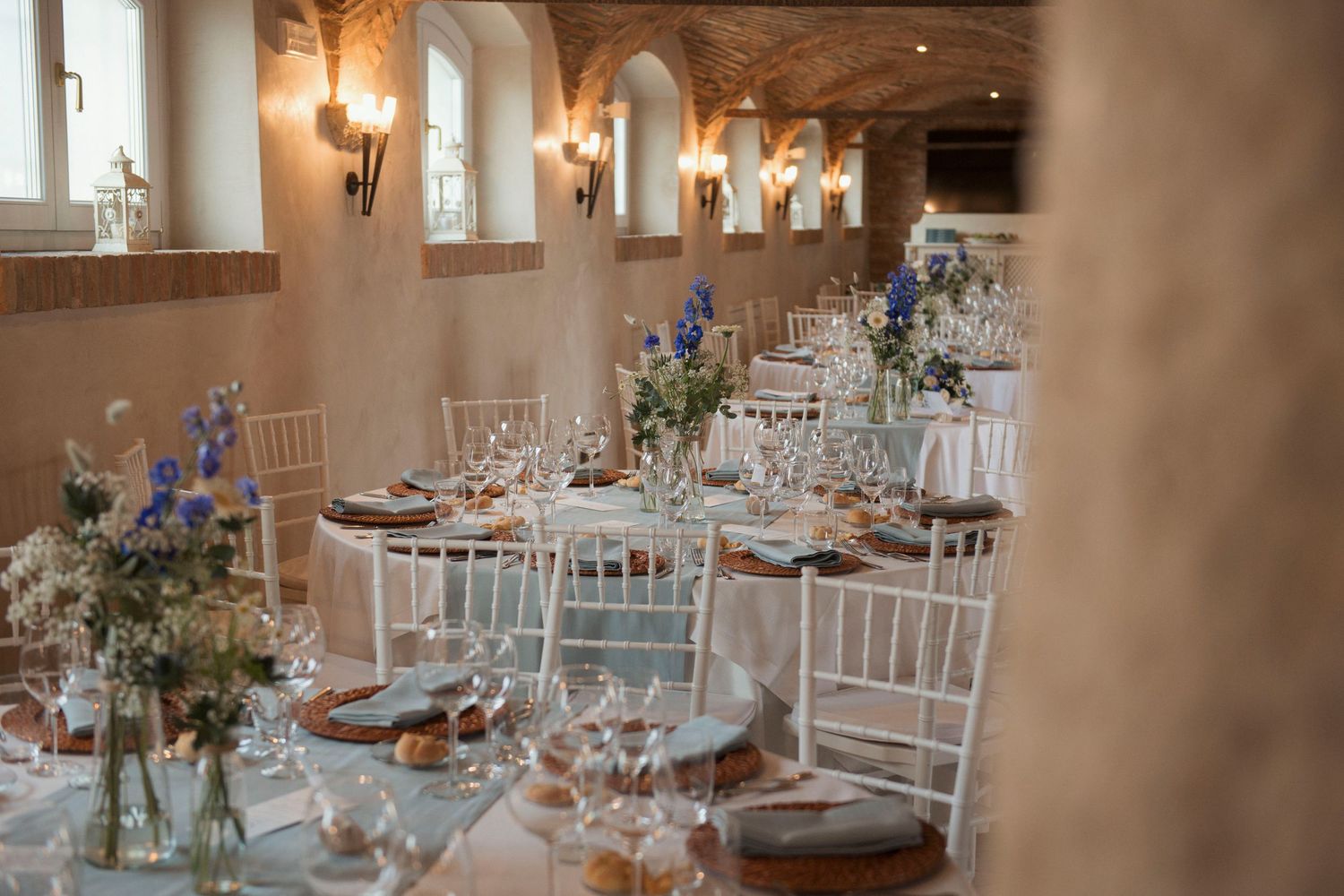 Elegant wedding reception hall with white Chiavari chairs, long tables, and blue floral centerpieces.