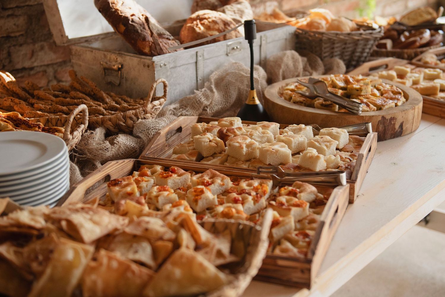 A buffet table displays an abundant spread of assorted pastries, breads, and finger foods arranged in wooden trays and baskets.