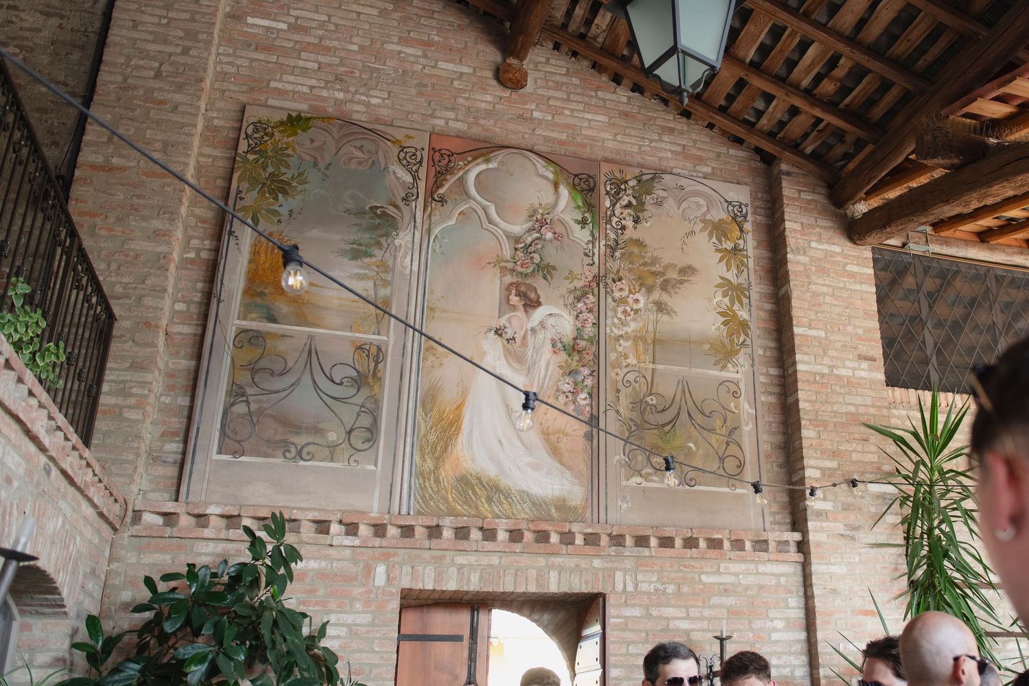 Ornate fresco mural painting on brick wall inside historic Italian courtyard building with arched details.