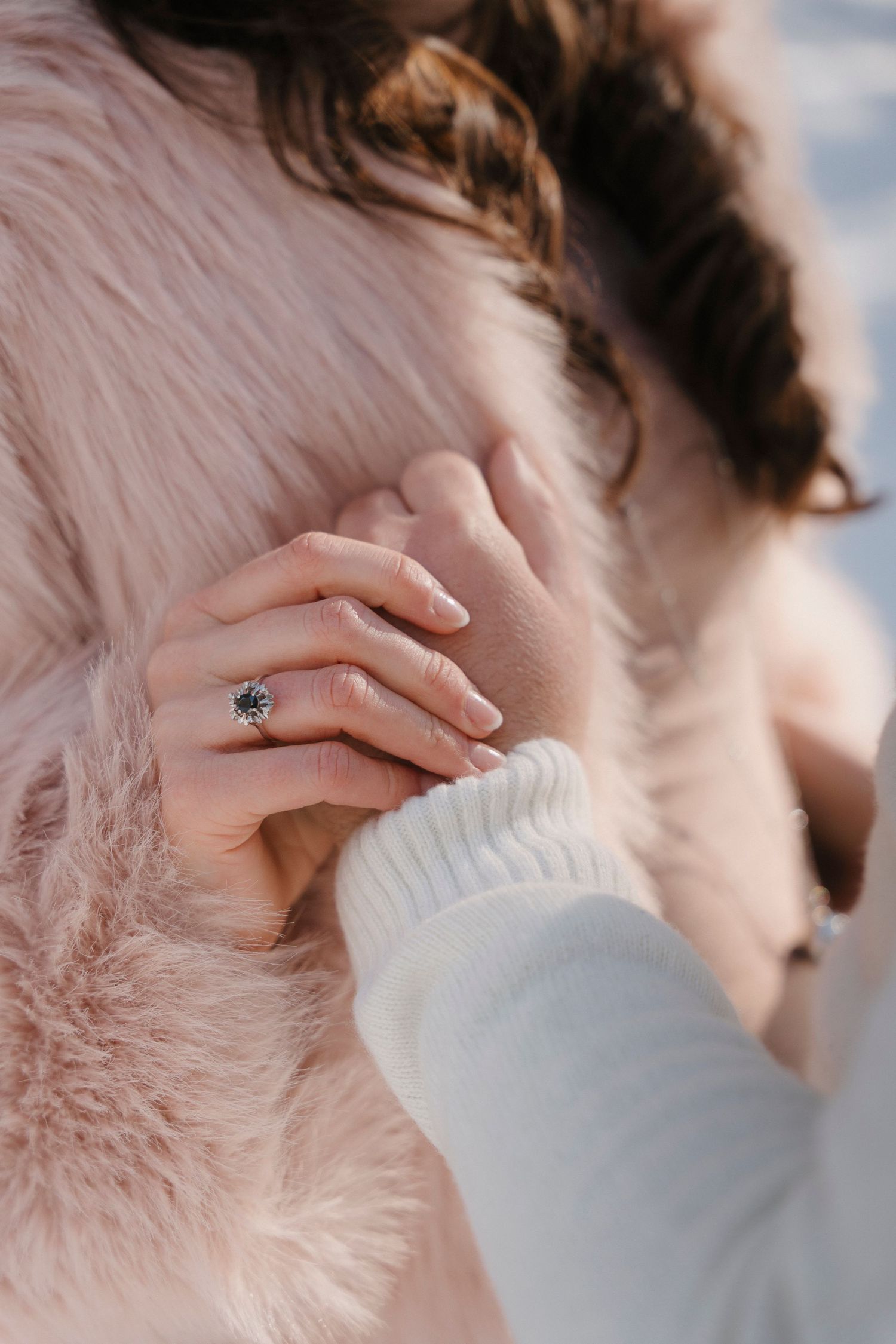 Close-up of woman's hand with a large round diamond ring resting on a pink fur coat.