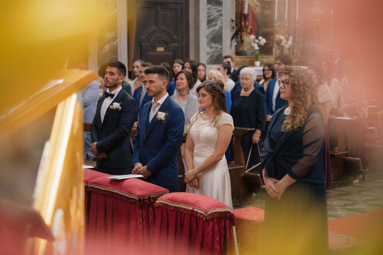 Bride and groom stand at the altar during a church wedding ceremony surrounded by guests in formal attire.