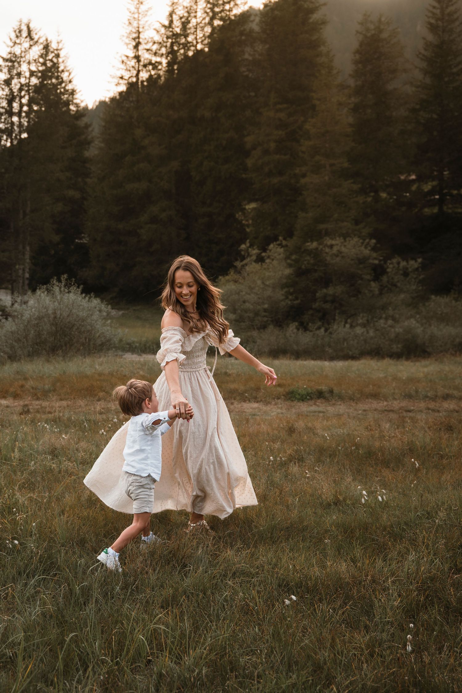 Mother and young son dancing playfully in green meadow at golden sunset.