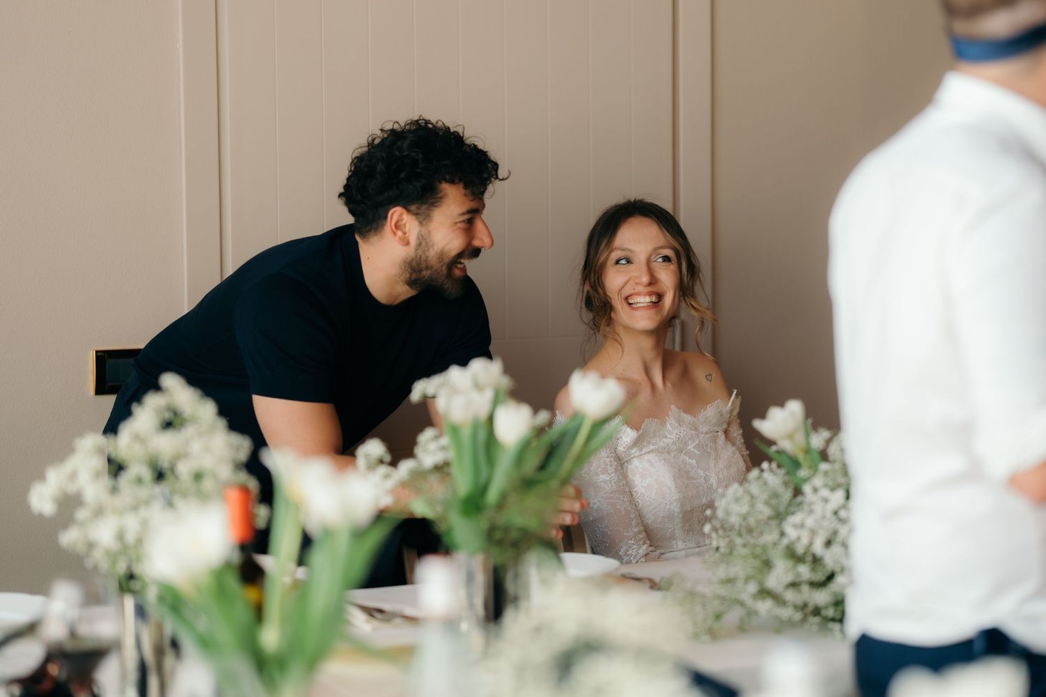 Bride and groom share a joyful moment at their wedding reception table surrounded by white tulip floral arrangements.