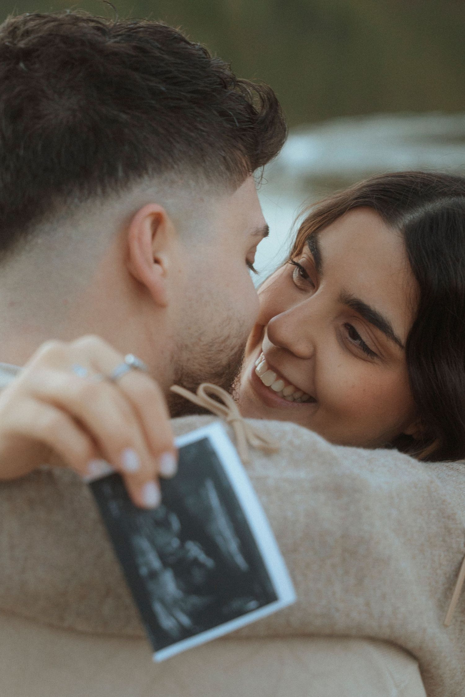 Couple smiling at each other while holding an ultrasound photo, announcing their pregnancy.