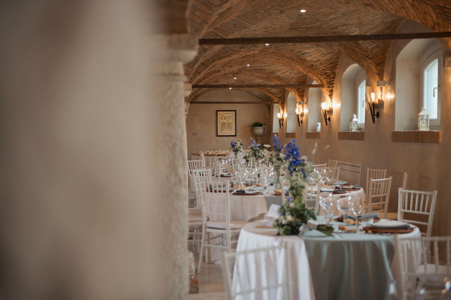 Elegant wedding reception hall with vaulted brick ceilings, white chiavari chairs, and floral centerpieces.