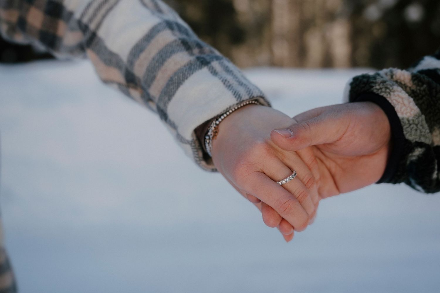 Close-up of couple holding hands in the snow, woman wearing a silver bracelet and ring.