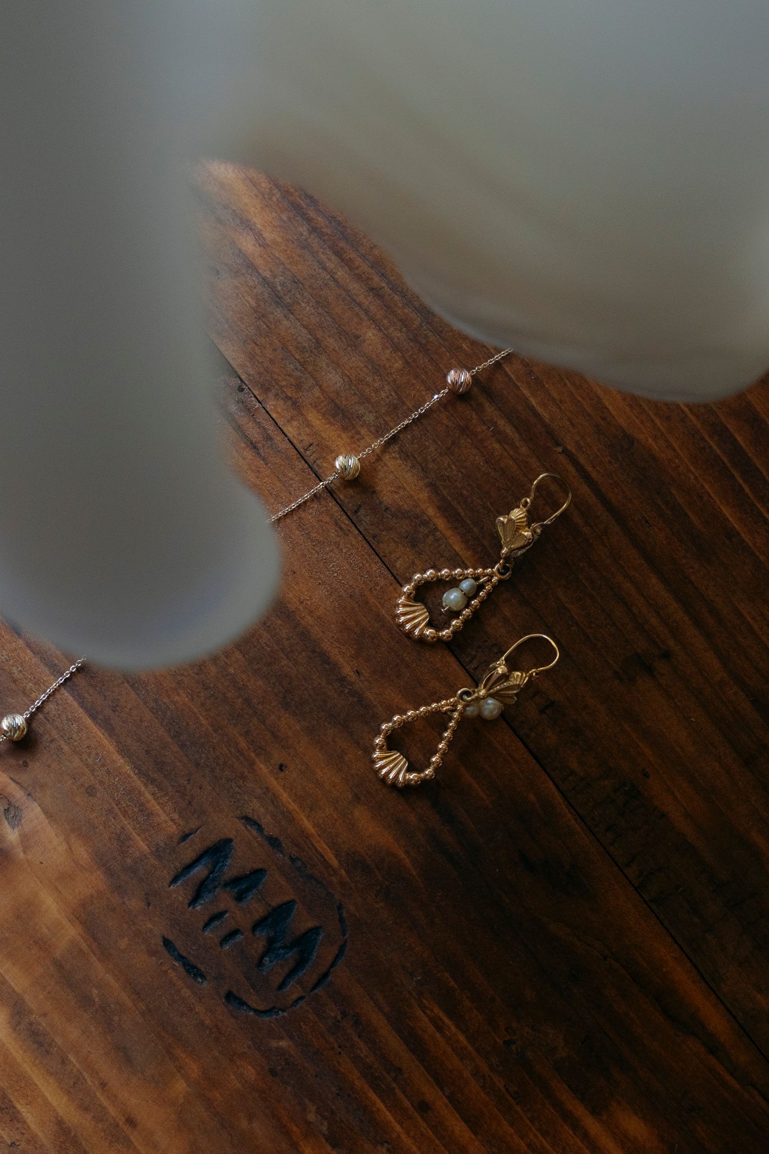 Gold teardrop earrings with gemstone details displayed on a dark wooden surface beside a bracelet.