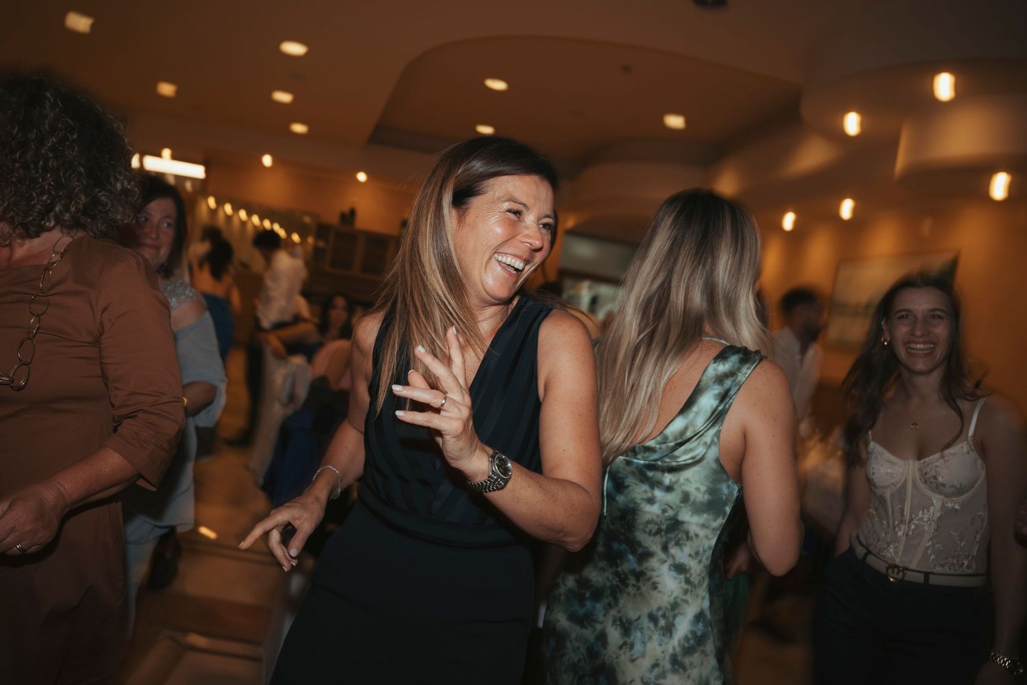 Women laugh and dance joyfully together on a crowded wedding reception dance floor.
