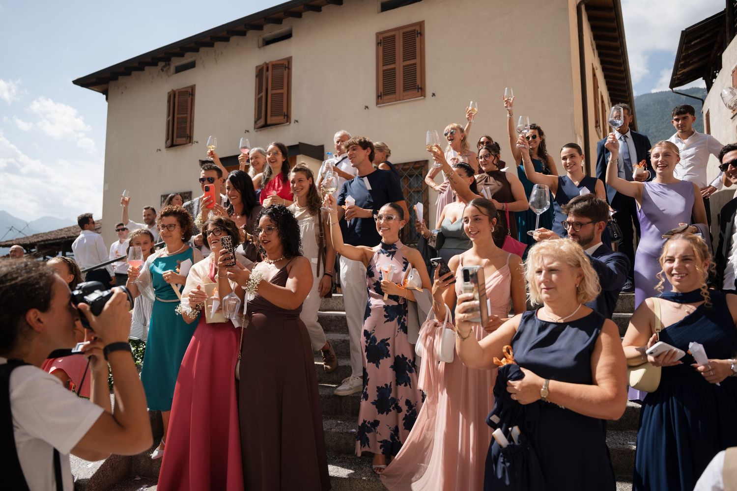Wedding guests celebrating outdoors on church steps in Italian village.
