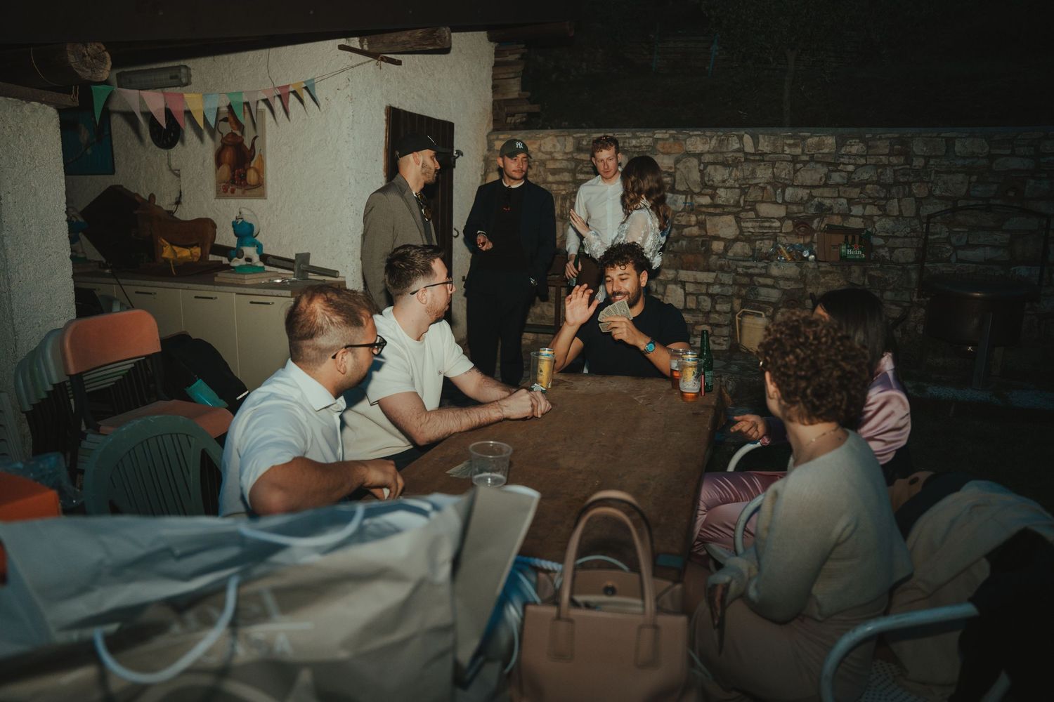 Group of people gathered around a table in a dimly lit stone room, engaged in lively conversation at an informal meeting.