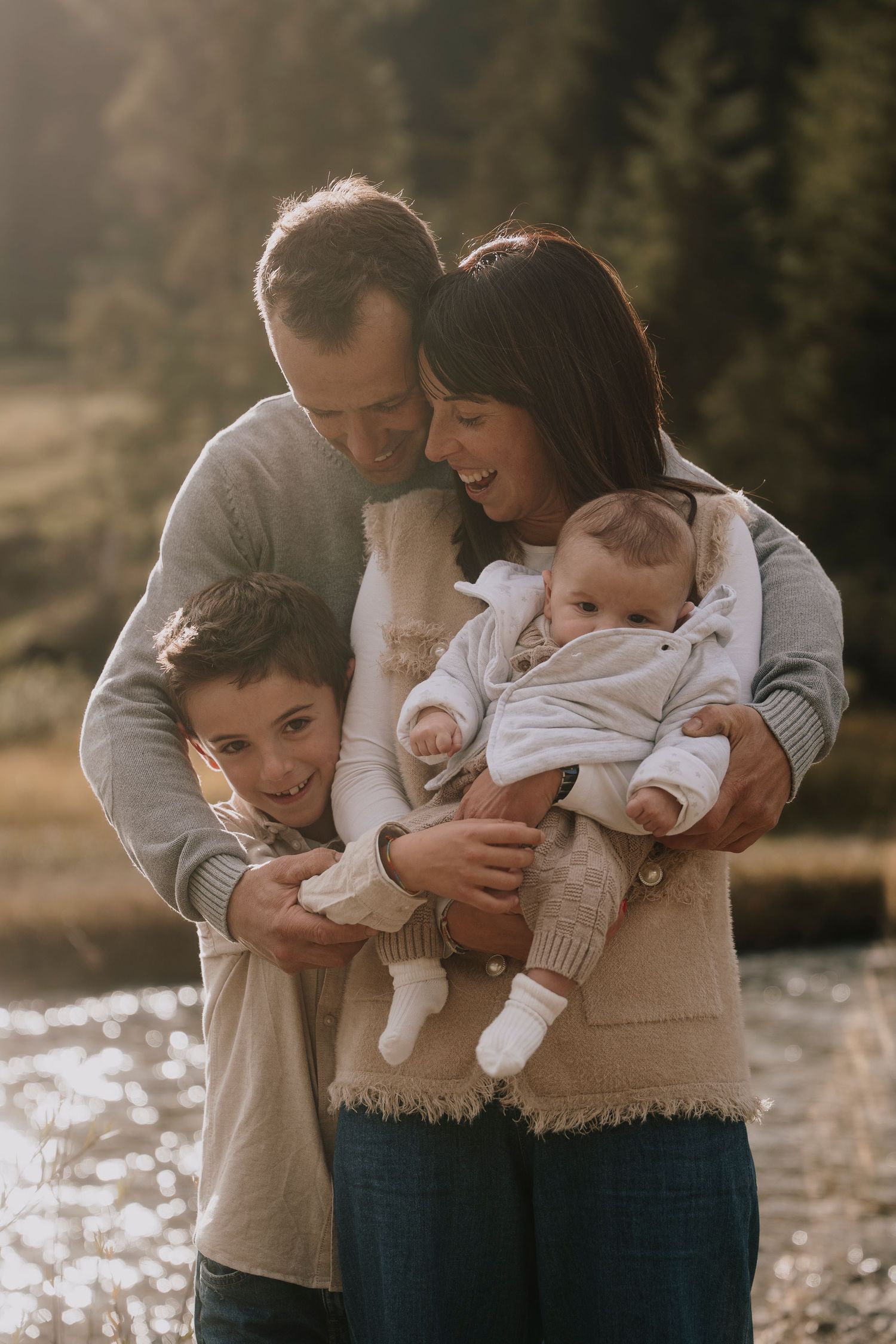Happy family of four with two children posing by a sunlit lake in autumn.