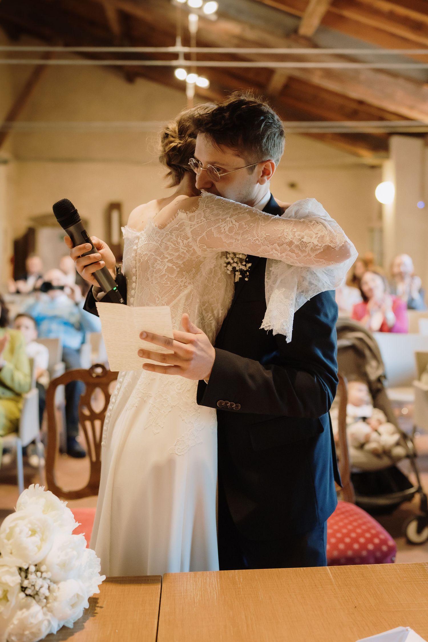 Bride and groom share emotional hug at altar during indoor wedding ceremony with guests.