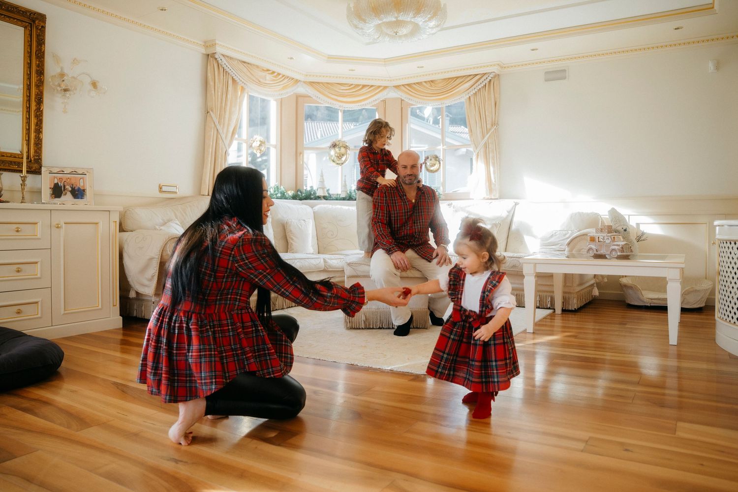 Family in matching plaid outfits playing together in bright elegant living room at Christmas.